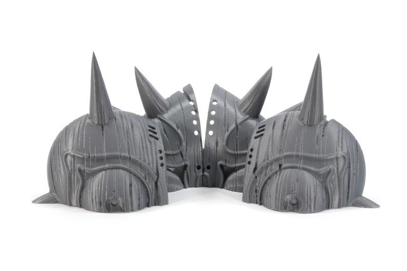 May include: Four gray 3D printed helmets with pointed horns. The helmets have a textured surface that resembles wood grain.