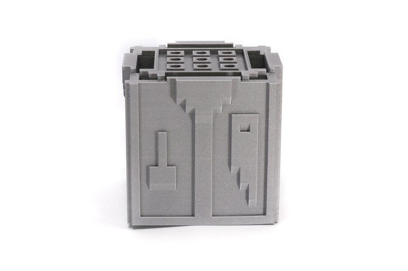 May include: A gray, cube-shaped storage box with a textured surface and a series of small holes on the top. The box has a unique design with geometric shapes on the front.