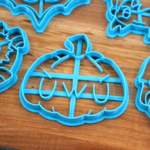 May include: A set of blue plastic cookie cutters shaped like a pumpkin, a skull, a bat, a monster, and a creature with a flower on its head. The pumpkin cutter has the word "uwu" inside.