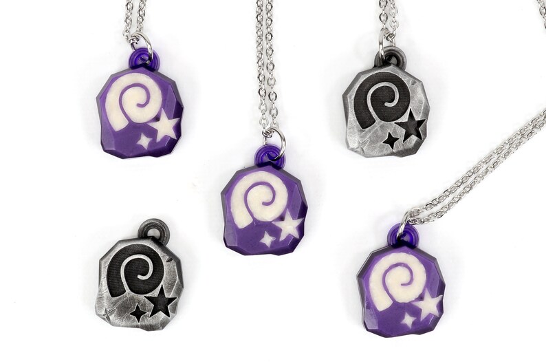 May include: Five necklaces with purple and silver pendants featuring a white spiral and two white stars. The pendants are shaped like a rock.