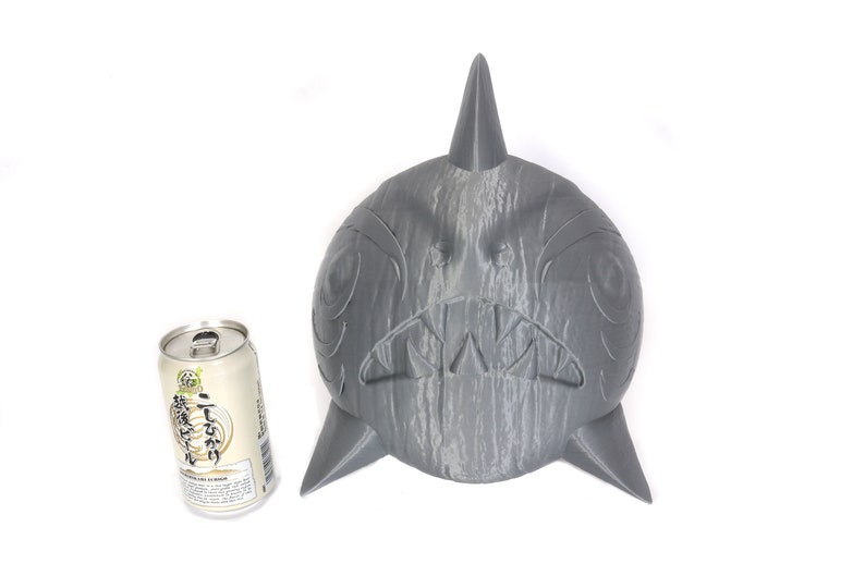 May include: A gray, wooden, carved shark head sculpture with a sharp fin on top. The sculpture is about the size of a standard can of soda.