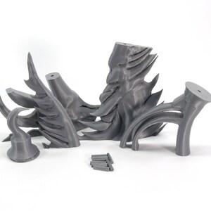 May include: A set of five gray 3D printed pieces that form a dragon sculpture. The pieces are arranged on a white surface.