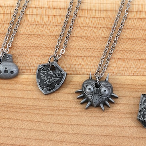 May include: Four silver necklaces with different pendants: an ocarina, a shield with a triforce symbol, a Majora's Mask, and a stone with a swirl design.