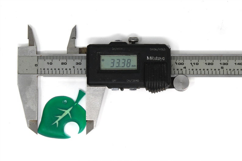 May include: A green leaf-shaped charm with a white stem and veins, measured with a digital caliper showing a measurement of 33.38 mm.