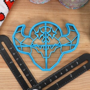 May include: A blue plastic cookie cutter shaped like a geometric monster with two stars on its head.