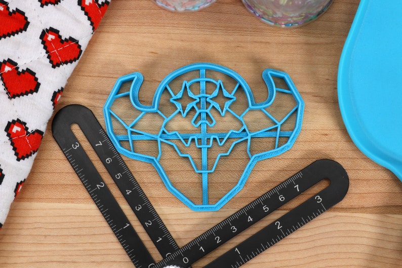May include: A blue plastic cookie cutter shaped like a geometric monster with two stars on its head.