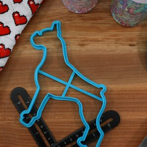 May include: A blue plastic cookie cutter shaped like a dog, on a wooden surface with a ruler and a blue spatula.
