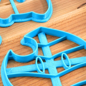 May include: Three blue plastic cookie cutters in the shape of a ghost, a snowman, and a Christmas tree. The cutters are on a wooden surface.