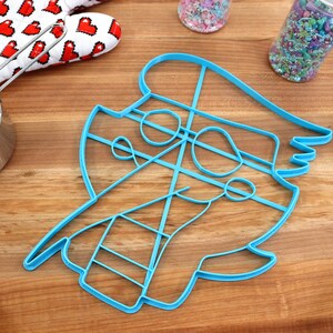 May include: A blue plastic cookie cutter shaped like a cartoon character with a hat. The cutter has a detailed design with lines and curves.