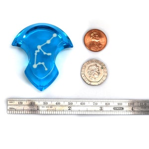 May include: A blue glass pendant with a white constellation design. The pendant is about 2 inches in diameter and is shown next to a ruler and two coins for scale.