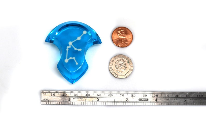 May include: A blue glass pendant with a white constellation design. The pendant is about 2 inches in diameter and is shown next to a ruler and two coins for scale.
