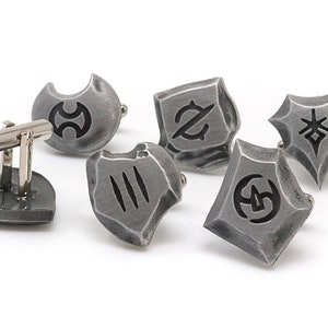 May include: Set of six silver cufflinks with different black symbols on each. The cufflinks are shaped like shields and have a textured surface.