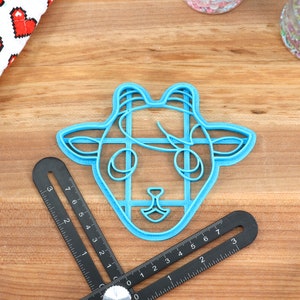 May include: A blue plastic cookie cutter shaped like a goat's head. The cutter has a detailed design with lines and curves.