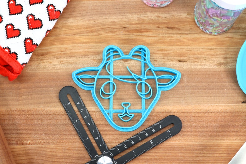 May include: A blue plastic cookie cutter shaped like a goat's head. The cutter has a detailed design with lines and curves.