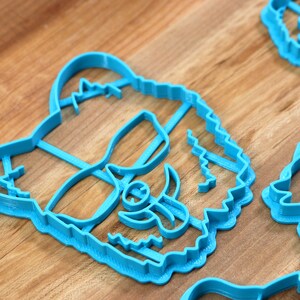 May include: A set of four blue plastic cookie cutters shaped like animal faces. The cutters are on a wooden surface.