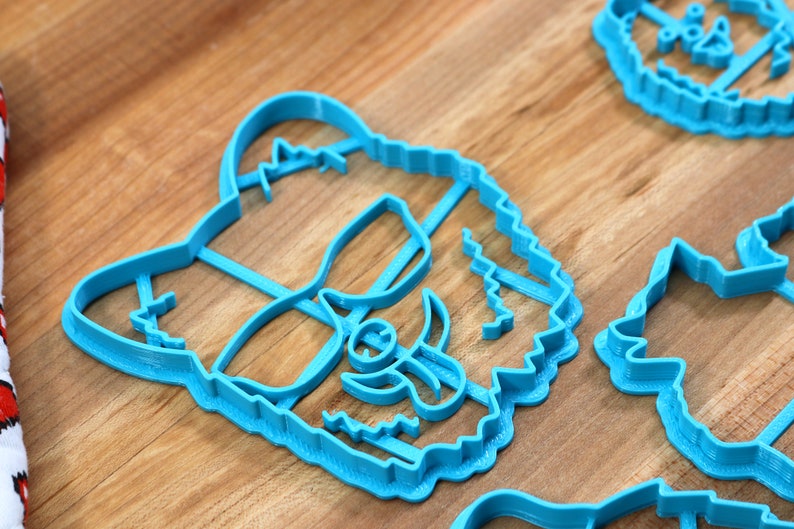 May include: A set of four blue plastic cookie cutters shaped like animal faces. The cutters are on a wooden surface.