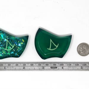 May include: Two green resin dice with a white symbol on each. One die has a glittery finish.