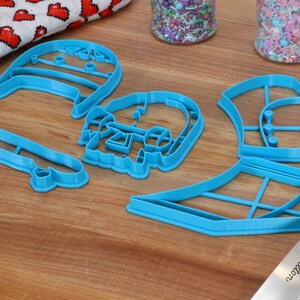 May include: A set of five blue plastic cookie cutters shaped like a skateboard, a skull, a hat, a surfboard, and a pair of headphones.