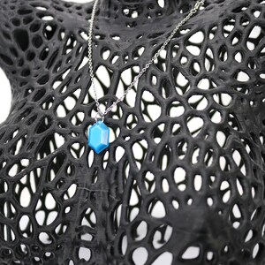 May include: A blue gemstone pendant necklace on a silver chain, displayed on a black 3D printed mannequin bust.