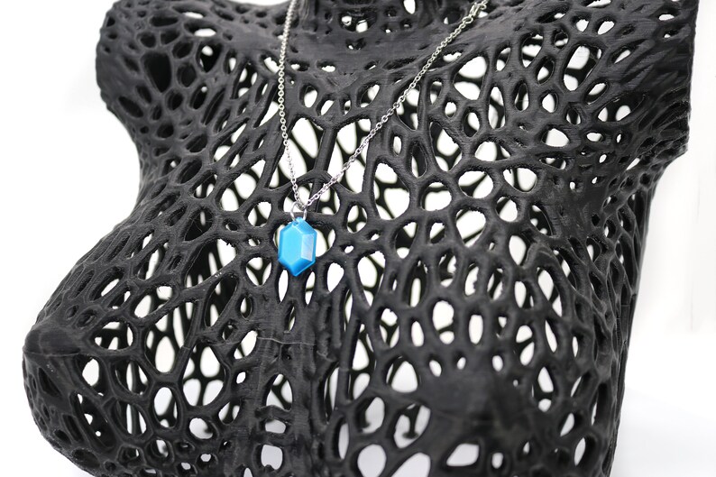 May include: A blue gemstone pendant necklace on a silver chain, displayed on a black 3D printed mannequin bust.