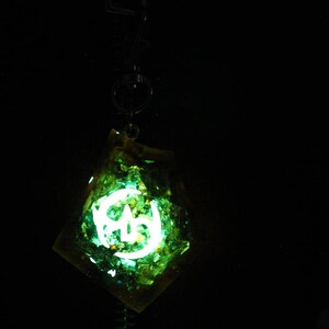May include: A green and yellow resin pendant with a glowing white symbol inside. The pendant is on a black chain.