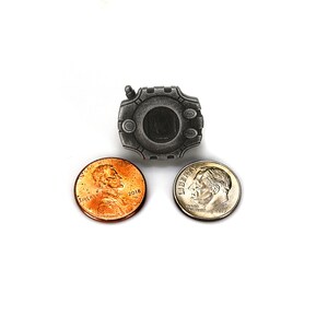 May include: A silver-colored metal pin shaped like a video game device with a black screen. The pin is surrounded by two US coins, a penny and a dime.