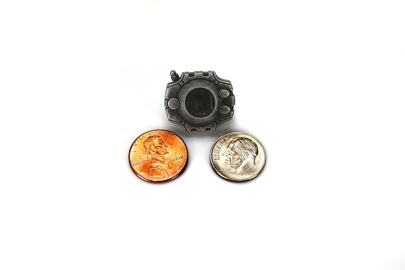 May include: A silver-colored metal pin shaped like a video game device with a black screen. The pin is surrounded by two US coins, a penny and a dime.