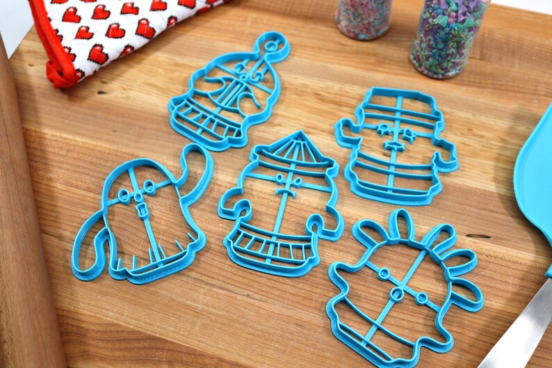 May include: A set of five blue plastic cookie cutters shaped like cartoon characters. The cutters are on a wooden surface.