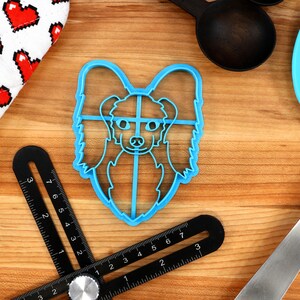 May include: Blue plastic cookie cutter shaped like a dog's head. The dog has long, flowing hair and a sweet expression.