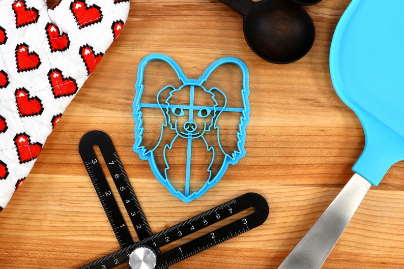 May include: Blue plastic cookie cutter shaped like a dog's head. The dog has long, flowing hair and a sweet expression.