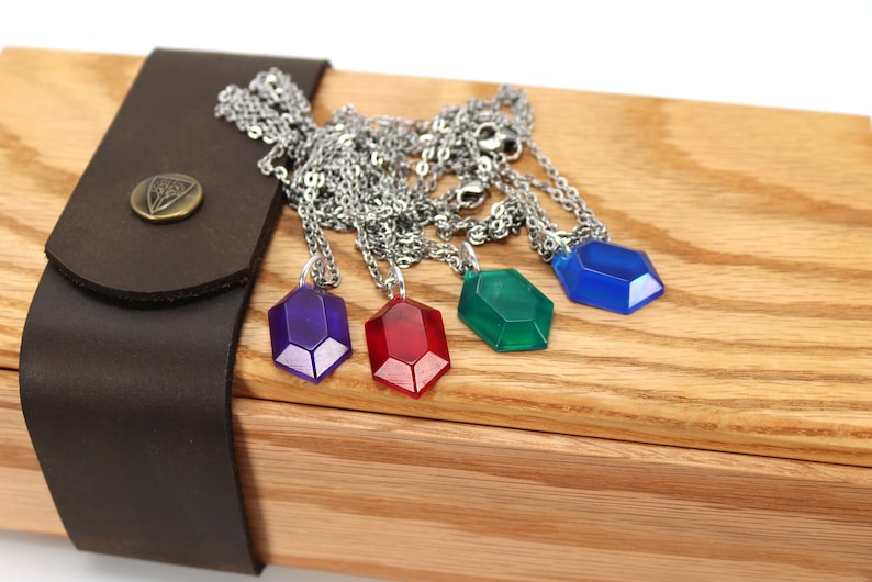 May include: Four necklaces with different colored gem pendants in a wooden box. The gems are purple, red, green, and blue.
