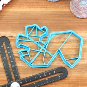 May include: A light blue plastic cookie cutter shaped like a geometric design. The cutter is on a wooden surface.
