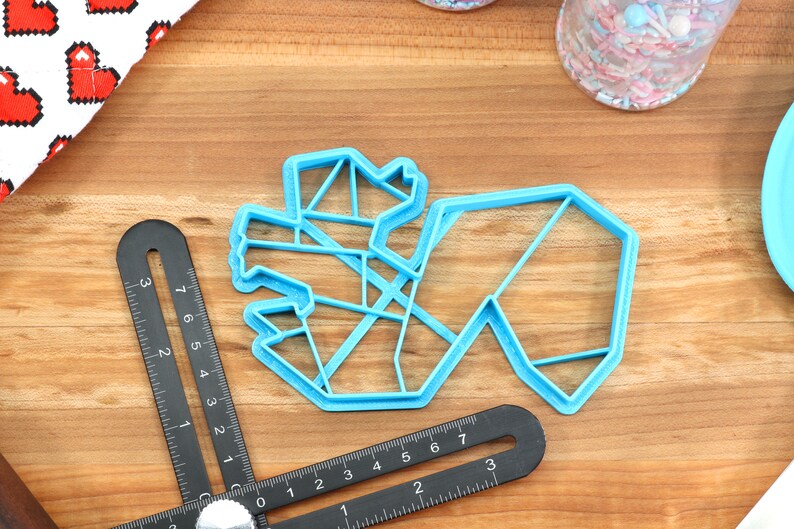 May include: A light blue plastic cookie cutter shaped like a geometric design. The cutter is on a wooden surface.
