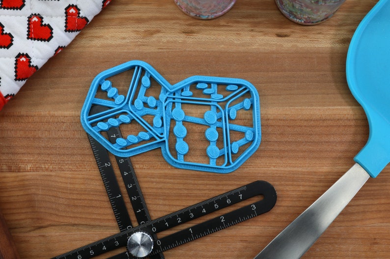 May include: Two blue plastic cookie cutters shaped like dice. The dice are joined together and have a textured surface.