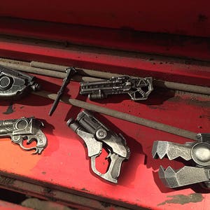 Puede incluir: Una colecci&oacute;n de cinco pistolas de juguete de color plateado, que incluyen una pistola, un rifle y un arma de aspecto futurista. Las armas est&aacute;n dispuestas sobre una superficie roja.