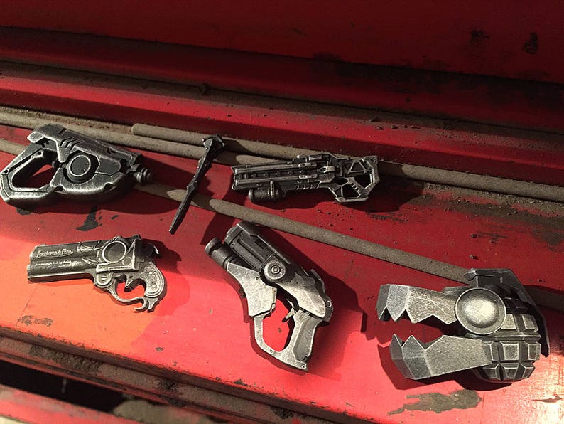 Puede incluir: Una colecci&oacute;n de cinco pistolas de juguete de color plateado, que incluyen una pistola, un rifle y un arma de aspecto futurista. Las armas est&aacute;n dispuestas sobre una superficie roja.