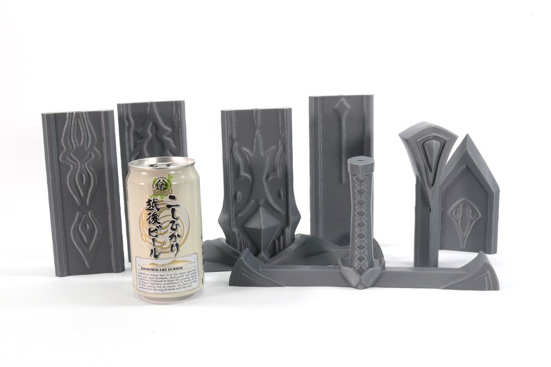 May include: A set of gray 3D printed pieces that can be assembled into a sword. The pieces are arranged on a white surface with a can of Japanese beer in the center.