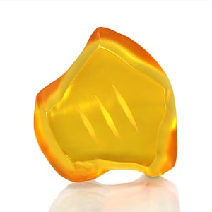 May include: A unique, abstract-shaped decorative object. The piece is a vibrant yellow with orange edges, and three diagonal lines are etched into the surface. The object is set against a white background, with a subtle reflection.