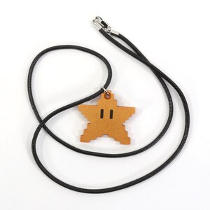May include: A black cord necklace with a gold star-shaped pendant. The star has a pixelated design and two black eyes.