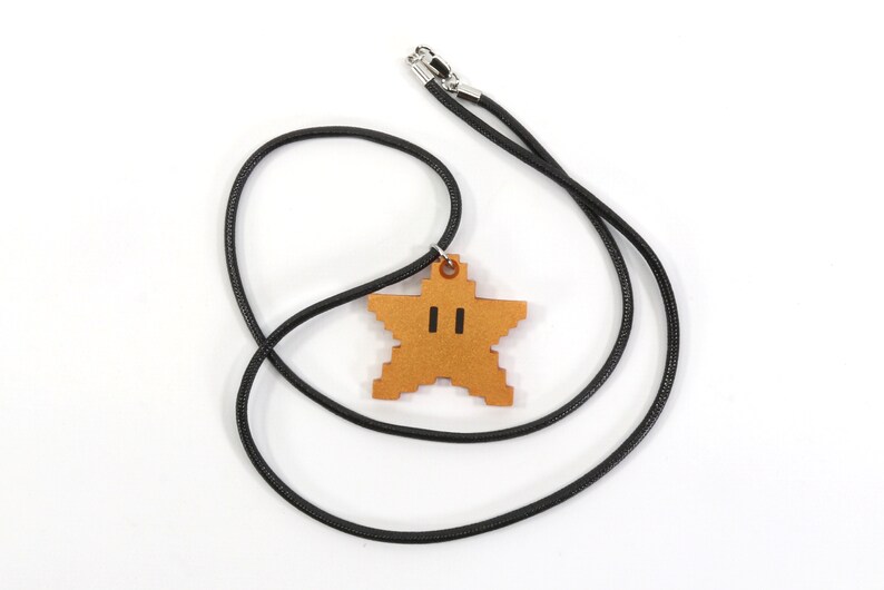 May include: A black cord necklace with a gold star-shaped pendant. The star has a pixelated design and two black eyes.