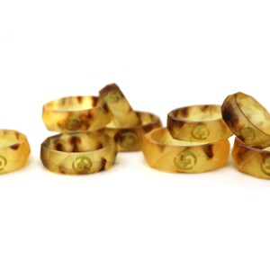 May include: A group of eight brown and yellow silicone rings with a gold logo. The rings are stacked and scattered on a white surface.