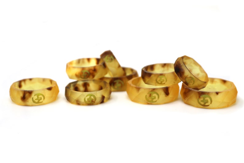 May include: A group of eight brown and yellow silicone rings with a gold logo. The rings are stacked and scattered on a white surface.