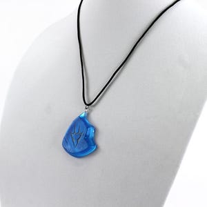 May include: A blue glass pendant necklace with a silver chain and a black cord. The pendant is shaped like a teardrop and has a silver design on it.