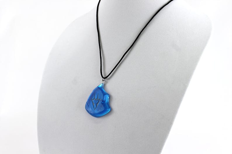 May include: A blue glass pendant necklace with a silver chain and a black cord. The pendant is shaped like a teardrop and has a silver design on it.