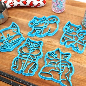 May include: Set of six blue plastic cookie cutters shaped like cartoon dogs. The cutters are on a wooden surface.