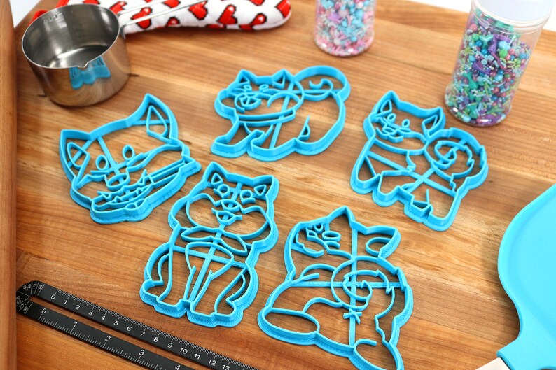 May include: Set of six blue plastic cookie cutters shaped like cartoon dogs. The cutters are on a wooden surface.