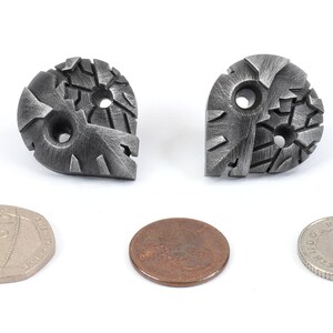 May include: Two silver metal buttons with a textured, geometric design. Each button has two holes for sewing. The buttons are about the size of a US penny.