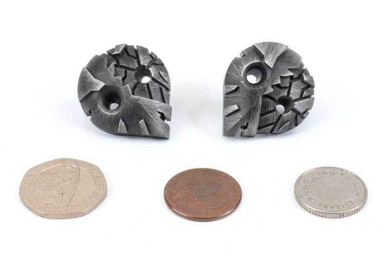 May include: Two silver metal buttons with a textured, geometric design. Each button has two holes for sewing. The buttons are about the size of a US penny.