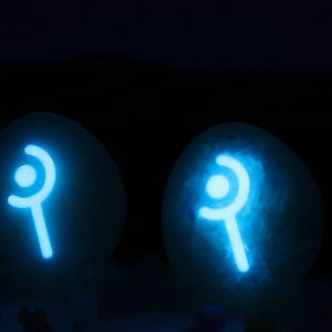 May include: Two white, round, glowing orbs with a blue, stylized symbol of a wand with a circle on top. The orbs are on a dark background.