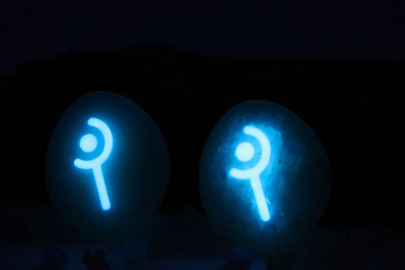 May include: Two white, round, glowing orbs with a blue, stylized symbol of a wand with a circle on top. The orbs are on a dark background.